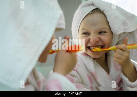 Bella ragazza in accappatoio con asciugamano nei suoi capelli spazzolare i denti Foto Stock