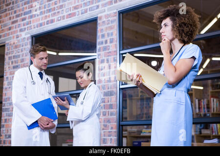 Femmina del pensiero medico mentre si verifica un file libreria vicino Foto Stock