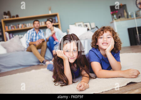 I bambini in appoggio sul tappeto mentre i genitori seduti in background Foto Stock