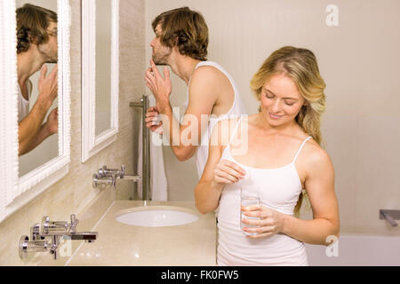 Donna bionda di prendere una pillola con il suo fidanzato spazzolando i suoi denti Foto Stock