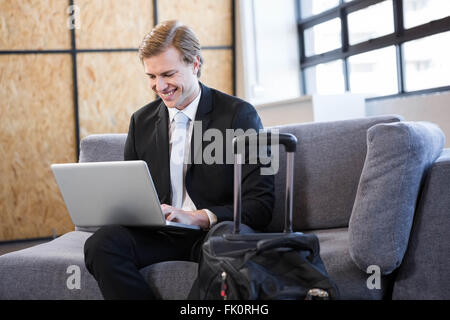 Happy businessman seduti sul divano e tramite computer portatile Foto Stock