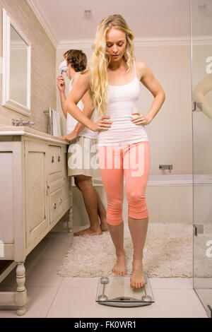 Donna bionda circa l'uso di una bilancia mentre il suo fidanzato la rasatura Foto Stock