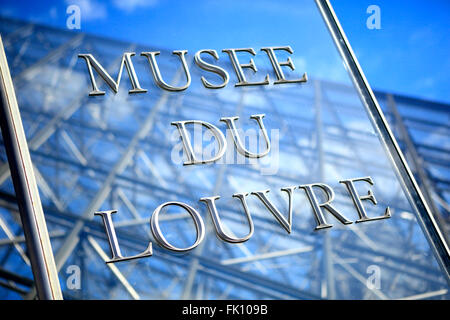 In vetro e acciaio inossidabile segno di entrata al Museo del Louvre a Parigi con parte della famosa piramide di vetro in background. Foto Stock