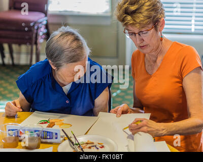 Una femmina la maestra insegna una femmina senior citizen di vernice in un acquerello di classe a un senior centre di Santa Barbara. Foto Stock
