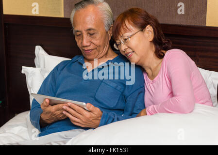 Asian giovane relax nel letto a guardare di intrattenimento su un tablet. Foto Stock