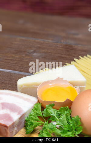 Sguardo l'angolo su ingredienti per i tradizionali spaghetti alla carbonara giacente su un olivo scrivania in legno. Verticalmente. Foto Stock