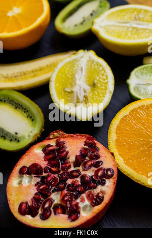 Fette di frutta esotica al buio su un bordo, kiwi, calce, limone, melograno, arancione categoricamente Foto Stock