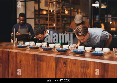 Barista training in un moderno roastery con i manager a prendere appunti Foto Stock