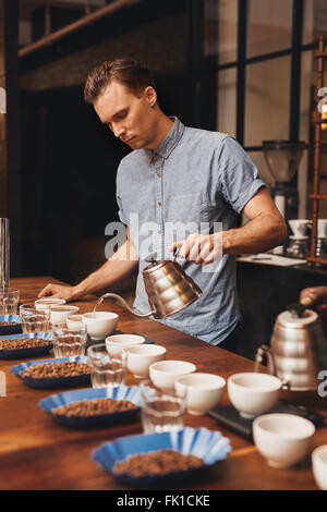 Barista preparazione per una degustazione di caffè con righe di tazze Foto Stock