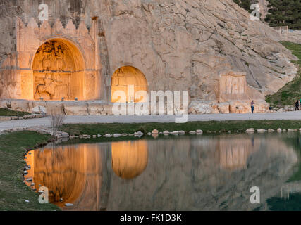 Vista serale di riflettori Taq-e Bostan Sassanide altorilievi come riflesso nel laghetto. Sito situato nei pressi di Kermanshah, Iran Foto Stock