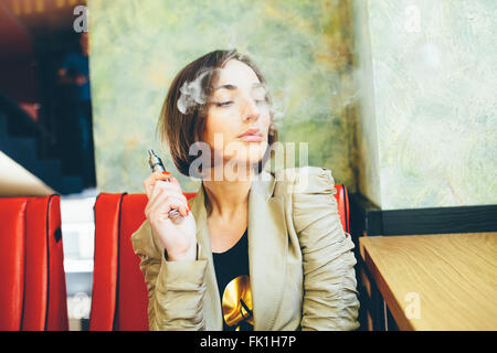 La ragazza si siede e fuma sigaretta elettronica Foto Stock