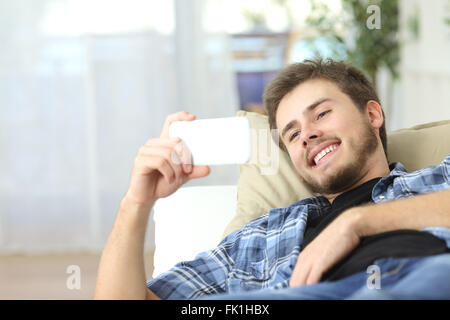 Uomo felice guardando un film in uno smart phone sdraiato su un lettino a casa Foto Stock