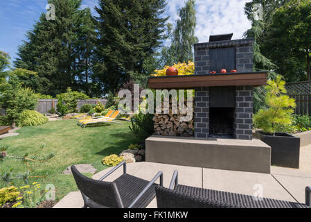 Un alto, personalizzata camino con mattoni grigi e abbondanza di legna da ardere siede su un invitante patio con un bellissimo paesaggio Foto Stock