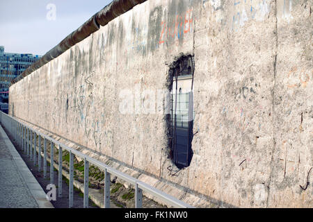 Celebre muro di Berlino il frammento protetto da recinzione metallica con focus sul foro grande Foto Stock