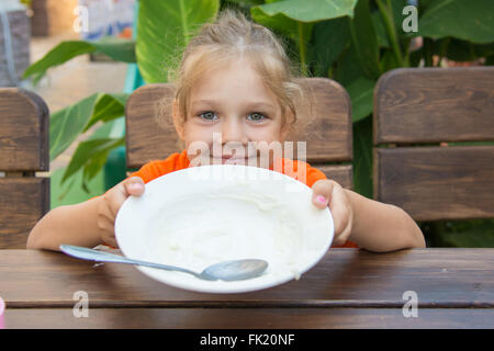 Cinque anni di ragazza mangiato tutto il porridge in una piastra e mostra una tazza vuota Foto Stock