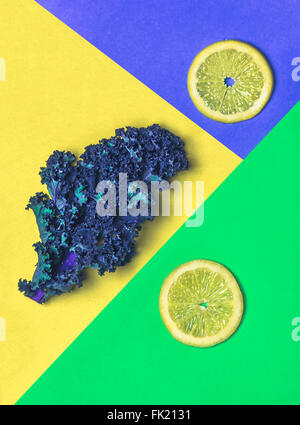 Fette di limone su blu e verde con cavolo verde su giallo Foto Stock