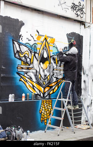 Un uomo su una scala la verniciatura a spruzzo approvato Wall Art Graffiti a Brick Lane London Foto Stock