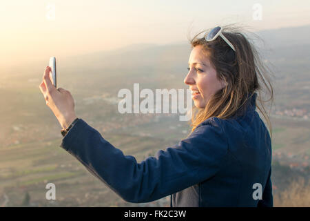 Ragazza tenendo un selfie su una escursione al tramonto Foto Stock