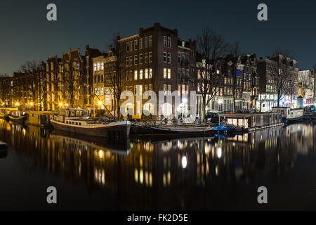 Una vista di edifici e barche lungo i canali di Amsterdam di notte. Riflessioni può essere visto nell'acqua. Non vi è lo spazio per la copia Foto Stock