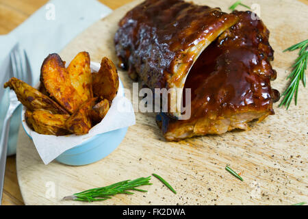 Nervature di barbecue con salsa, Spicchi di patate e spezie su un vassoio in legno Foto Stock