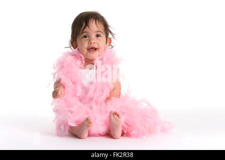 Baby ragazza seduta sul pavimento vestito in rosa piume come una diva su sfondo bianco Foto Stock