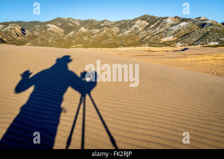 Un fotografo le riprese - ombra di un fotografo con una videocamera e treppiede su una duna di sabbia Foto Stock