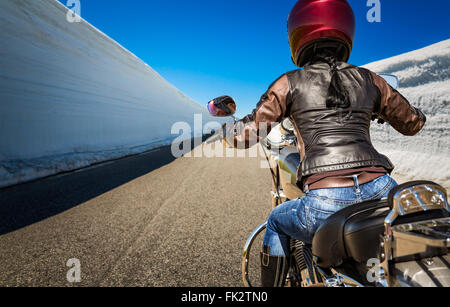 Biker ragazza scorre una strada di montagna con neve alta parete in Norvegia. Visuale in prima persona. Foto Stock