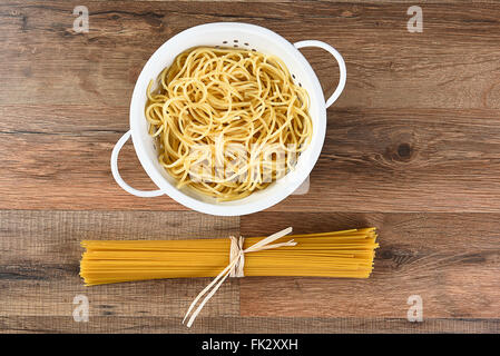 Vista aerea del cotto e spaghetti secchi. La pasta cotta è in uno scolapasta e le materie prime è legata con rafia. Orizzontale su un Foto Stock