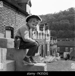 Ragazzo che gioca da solo con una catapulta e indossa un abito da cowboy con scarpe paraurti e pistola giocattolo anni '1960, via britannica fuori dalle strade Foto Stock