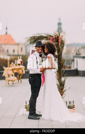 Nero allegro sposa e lo sposo tenendo le mani sulla cerimonia di nozze sul tetto Foto Stock