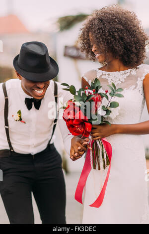 Un elegante nero groom nel cappello e la sua affascinante sposa felicemente ridere sul loro cerimonia di nozze Foto Stock