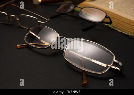 Occhiali con lenti di ingrandimento sulla superficie scura con i libri. Foto Stock