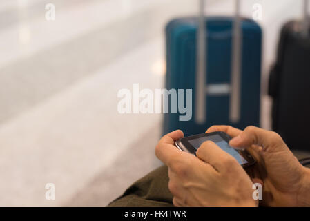 Messa a fuoco selettiva e close up di mani umane su smart phone con bagagli fuori fuoco nel terminal dell'aeroporto. Concetto di persone tra Foto Stock