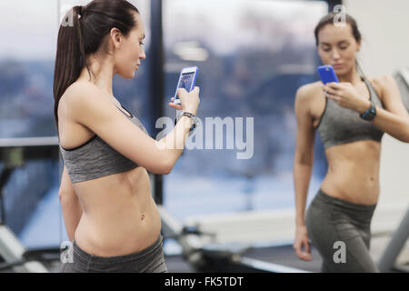 Donna con lo smartphone tenendo lo specchio selfie in palestra Foto Stock