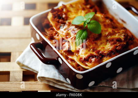 Il cibo italiano. Gustosi piatti caldi appena sfornati serviti di lasagne con basilico cantato sul tavolo di legno. Close-up, il fuoco selettivo. Foto Stock