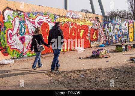 Giovane tenendo le mani a piedi passato coperto di graffiti muro di Berlino a Mauerpark, Berlino Foto Stock