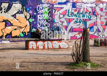 Coperto di graffiti muro di Berlino e il giovane uomo che dorme sul banco a Mauerpark, Berlino Foto Stock