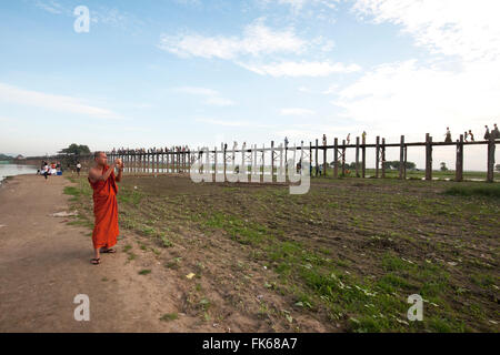 Orange derubato Monaco di fotografare le persone che attraversano le U Bein's Bridge supportato da 984 posti in teak oltre Thaumthaman Lago, Mandalay Foto Stock