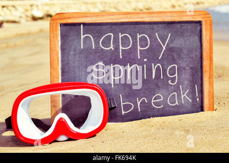 Primo piano di una di colore rosso e bianco maschera subacquea e il testo happy spring break scritto in un legno-incorniciato lavagna, sulla sabbia di una b Foto Stock