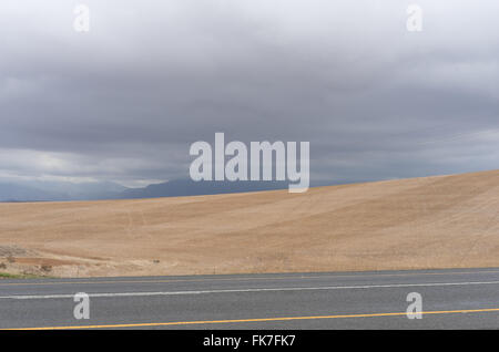 Raccolte di campi di grano in un giorno nuvoloso con montagne in lontananza Foto Stock