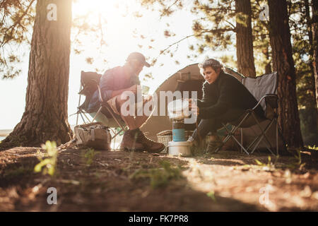Coppia senior per la cottura e la preparazione degli alimentari all'aperto su un viaggio di campeggio. Uomo maturo e la donna seduta al di fuori della tenda in un giorno di estate Foto Stock
