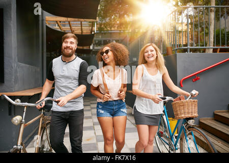 Tre giovani adulti camminare insieme avendo divertimento. I giovani con le biciclette passeggiate all'aperto in città. Foto Stock