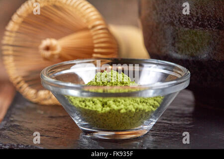 Verde matcha tè e una frusta sulla pietra nera piastra su una tavola di legno Foto Stock