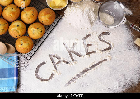 La parola scritta dolci di farina al buio su un tavolo di legno con Muffin appena sfornati e ingredienti. Foto Stock