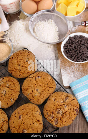 Appena sfornati i biscotti al cioccolato al buio su un tavolo di legno con spolverata di farina e ingredienti. Foto Stock