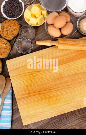 Appena sfornati i biscotti al cioccolato al buio su un tavolo di legno con tagliere e ingredienti. Foto Stock