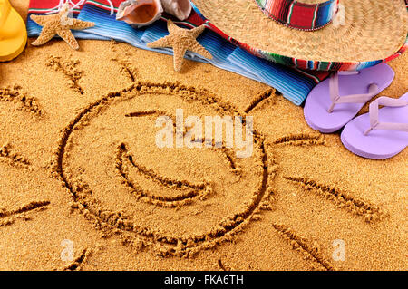 Sun sorridente disegnato in sabbia su una spiaggia messicana, con sombrero, cappello di paglia, tradizionale serape coperta, stelle marine e conchiglie. Foto Stock
