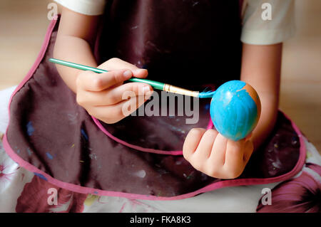 Uovo di Pasqua di essere verniciati con colore blu chiaro. Ragazza mani spazzola di vernice e uova in guscio. Messa a fuoco selezionata sull'uovo. Foto Stock