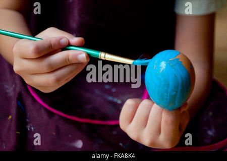 Uovo di Pasqua di essere verniciati con colore blu chiaro. Ragazza mani spazzola di vernice e uova in guscio. Messa a fuoco selezionata sull'uovo. Foto Stock