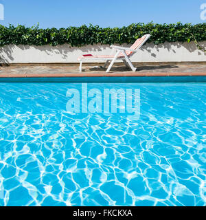 Ripples in piscina con edera sul muro e cielo blu e sedia a sdraio in background Foto Stock